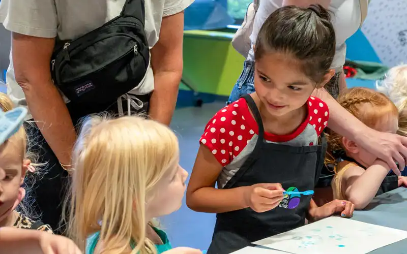 Children working on art projects at a table with an adult supervisor