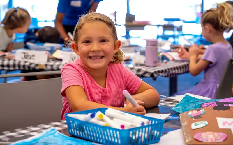 Smiling child at a table with educational materials and supplies